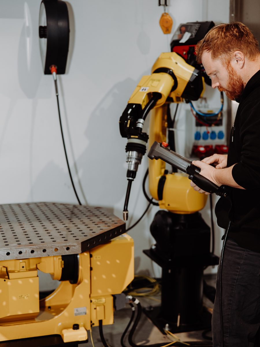 Fanuc Schweißroboter mit Positionierer, ein Mitarbeiter bedient das Programmiergerät
